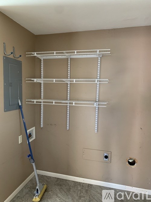 A room with a wall-mounted shelving unit and a broom.