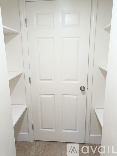 A white door with a silver handle is in a white room.