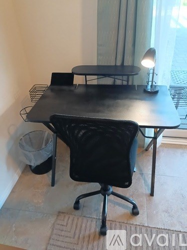 A black office chair is in front of a black table with a lamp on it.