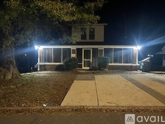 A house with a front yard and a driveway is illuminated by outdoor lights at night.