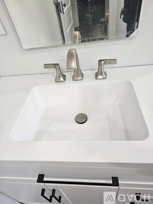 A white sink with a silver faucet and a mirror above it.