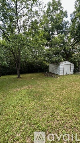 A shed sits in a grassy field with trees in the background.