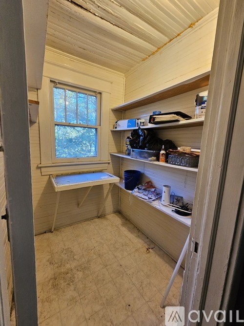 A small, white room with a window seat and a shelf with various items on it.