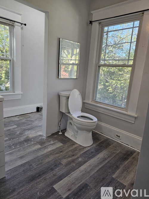 A bathroom with a toilet, a window, and a painting on the wall.