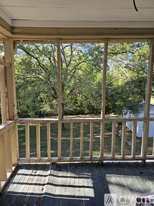 A wooden deck with a railing and a view of trees and a house.