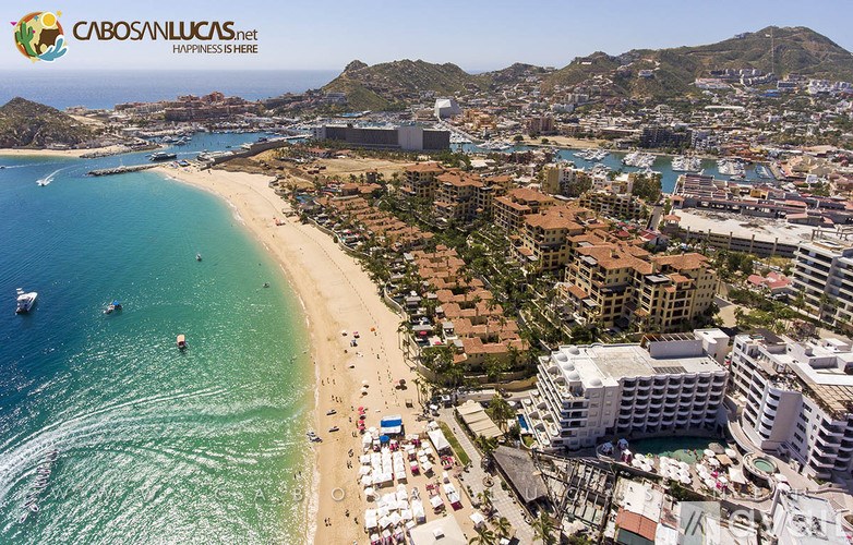A beachfront view of a resort with a clear blue sea and a mountain in the background.