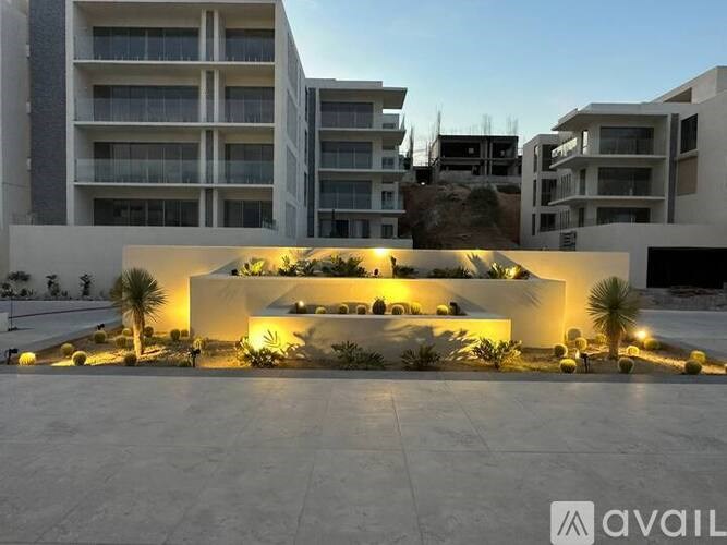 A modern building with a white facade and a garden in front is illuminated by warm lights.