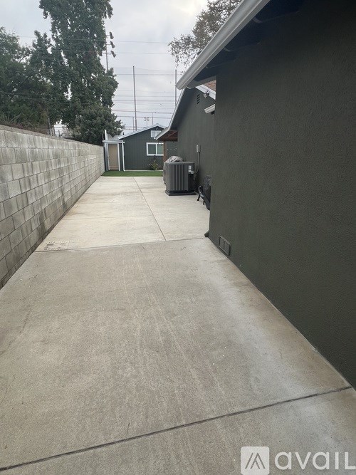 A concrete driveway leads to a house with a grey wall on the side.