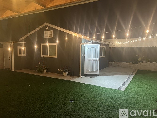 A house with a white door and windows is illuminated by string lights.