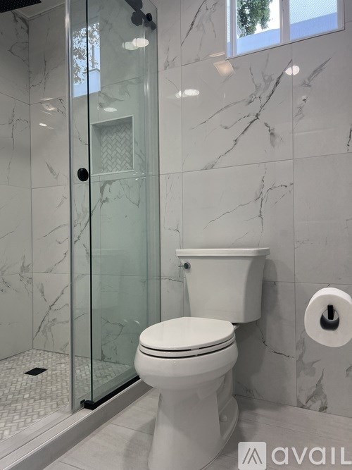 A white toilet in a marble tiled bathroom with a glass shower door.