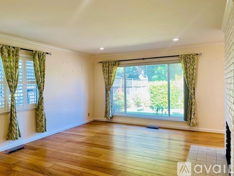 A room with wooden floors and a large window with curtains.