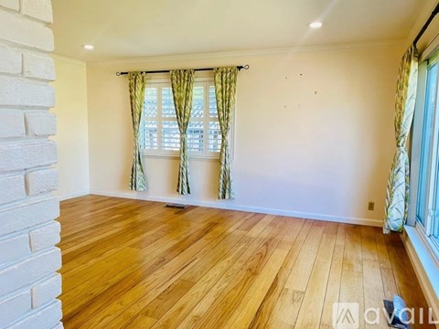 A room with wooden flooring and a window with green curtains.