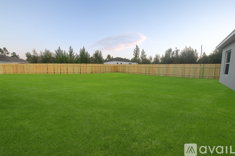 A large grassy field with a wooden fence and trees in the distance.