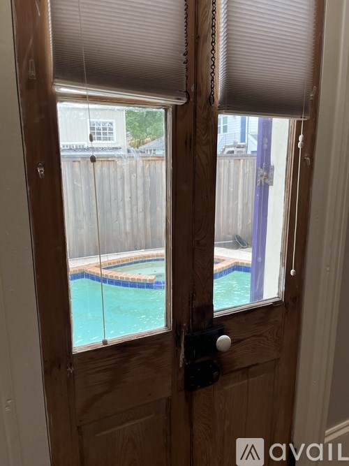 A wooden door with a black handle and a window with blinds overlooking a pool.