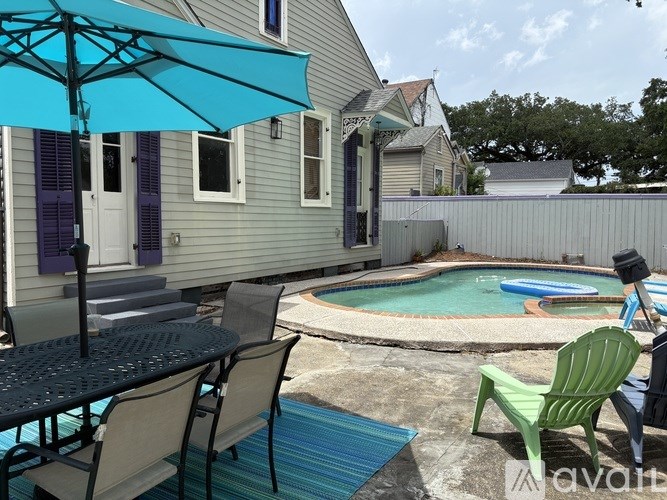 A patio with a table, chairs, and an umbrella overlooking a pool.