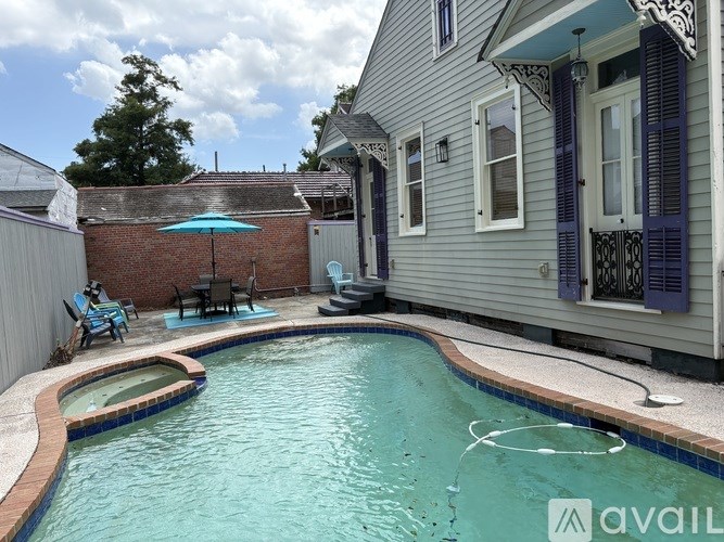 A pool in a backyard with a house and patio furniture.