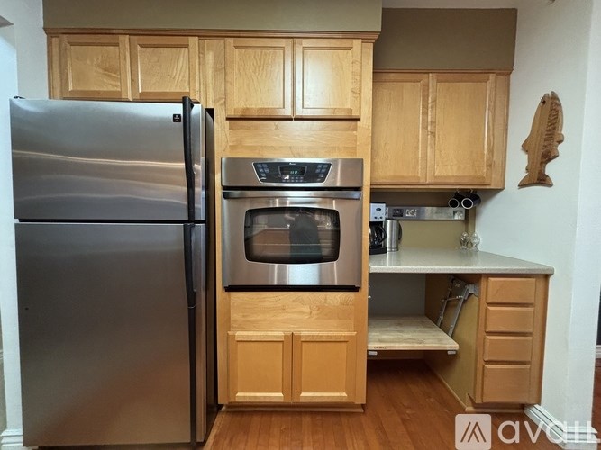 A kitchen with a stainless steel refrigerator and oven, wooden cabinets, and a pull-out drawer.