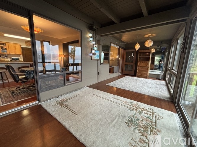 A living room with a rug on the floor and a kitchen area in the background.