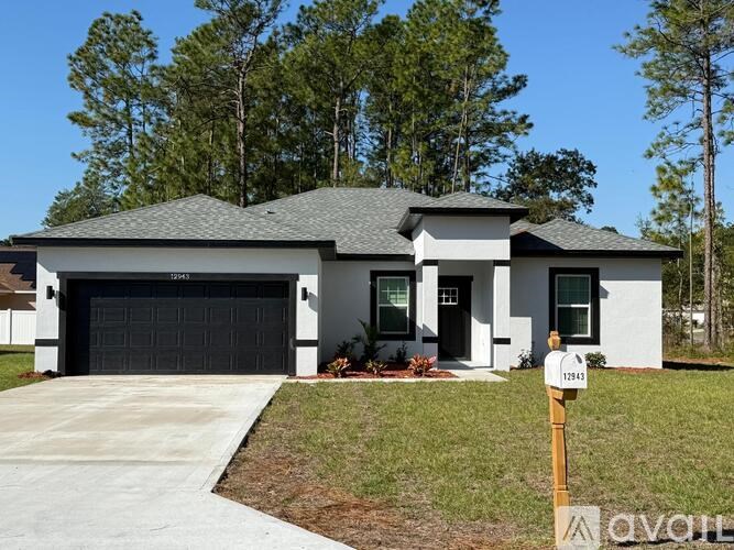 A white house with a black garage door is surrounded by trees.
