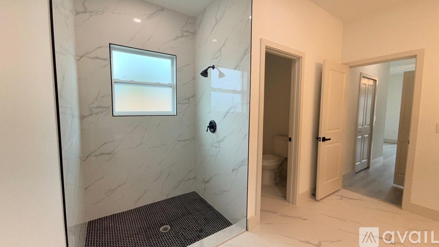 A bathroom with a marble wall and floor, a walk-in shower, and a window.