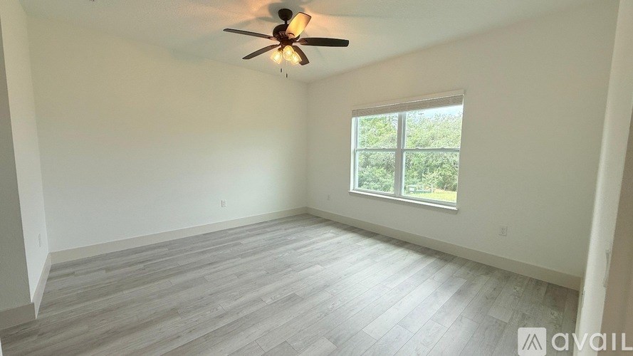 A room with a ceiling fan and a window overlooking greenery.