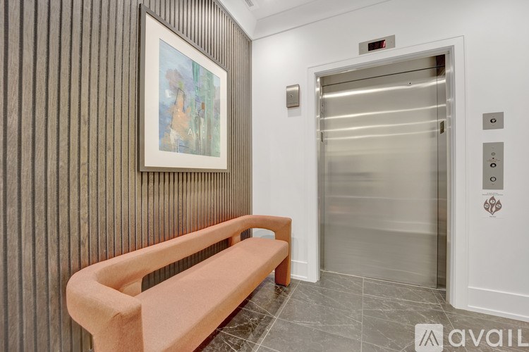 A hallway with a bench, a painting, and an elevator.