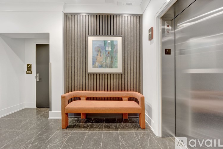 A long wooden bench sits in front of a wall with a painting and a silver elevator.