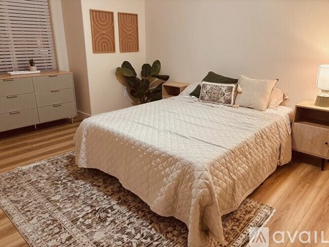 A bedroom with a bed, nightstand, and a plant.