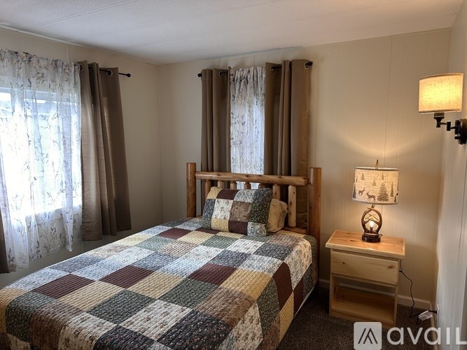 A bedroom with a bed, nightstand, and window with curtains.