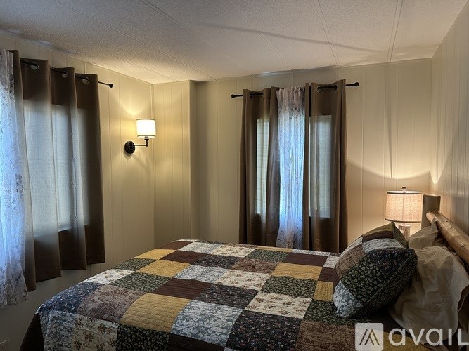 A bedroom with a bed covered in a quilt and two wall lamps.