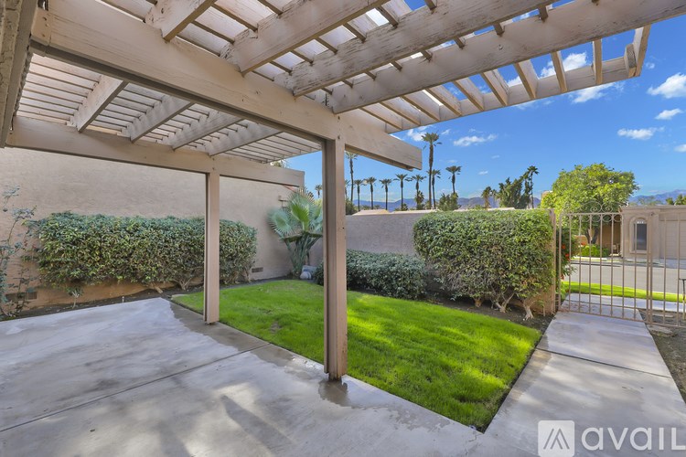 A patio with a wooden pergola and a concrete floor.