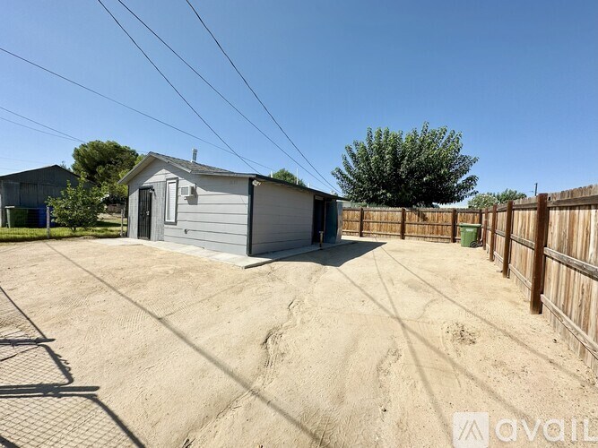 A grey metal shed sits in a sandy backyard.