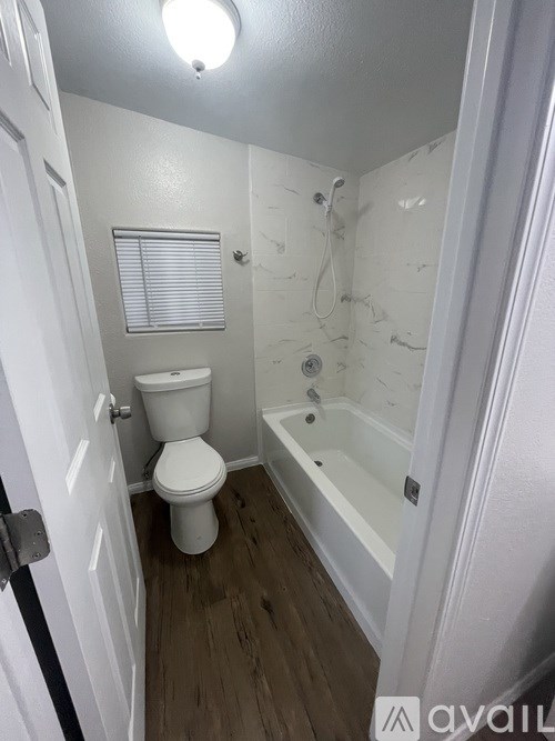 A white toilet is in a bathroom with a bathtub and a window.