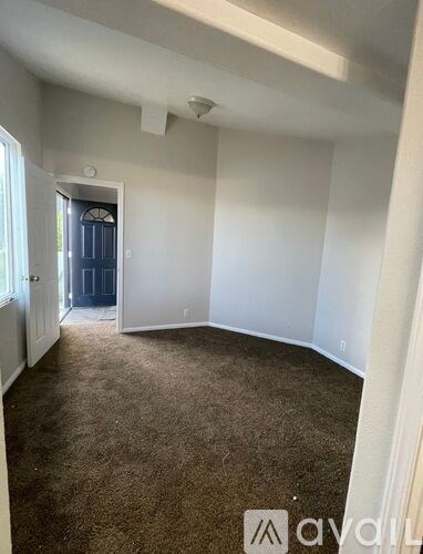 A room with white walls and carpeted floor with a doorway leading to another room.