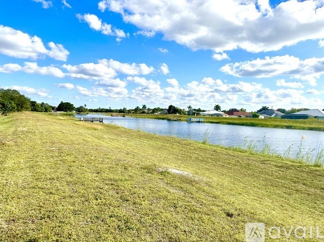 A grassy field with a body of water and a cloudy sky.