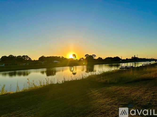 A sunset over a lake with a reflection in the water and a house in the distance.