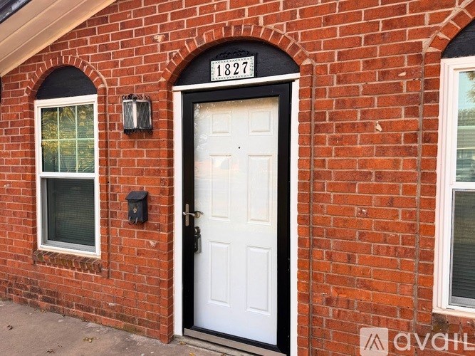 A white door with a black handle is on a brick wall with a number 1827 on it.