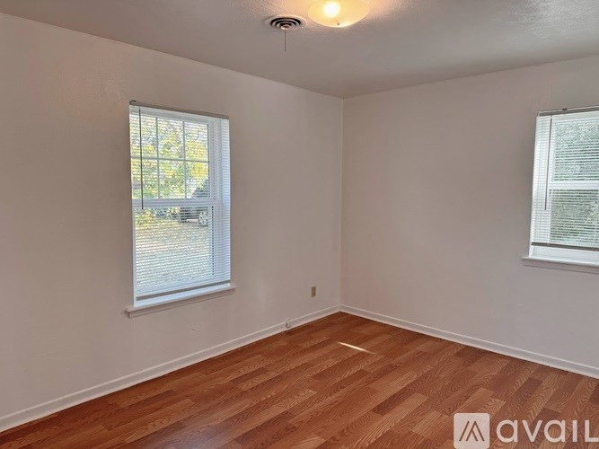 A room with wooden flooring and two windows.