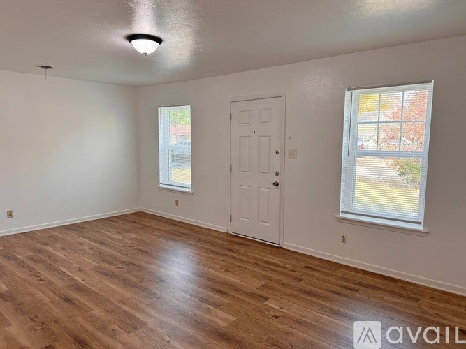 A room with wooden flooring and two windows.