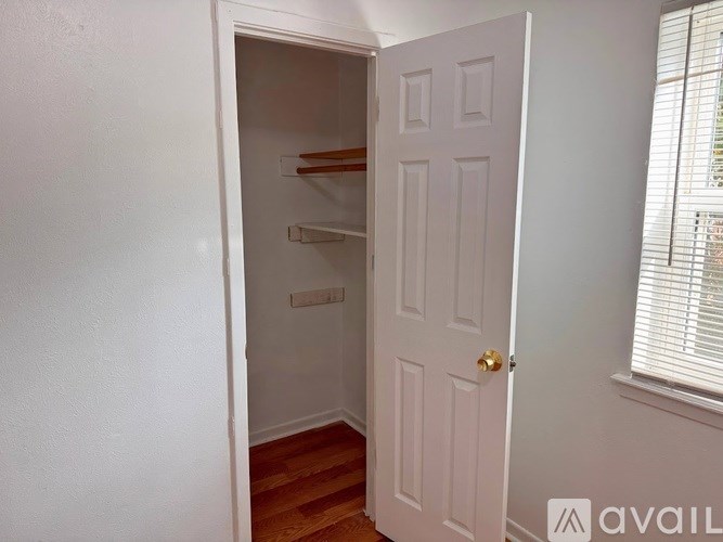 A white door with a gold handle is open to a small pantry with a shelf and a window with blinds.