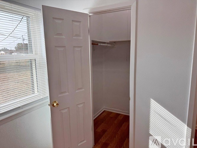 A white door is open to a small, empty room with wooden flooring.