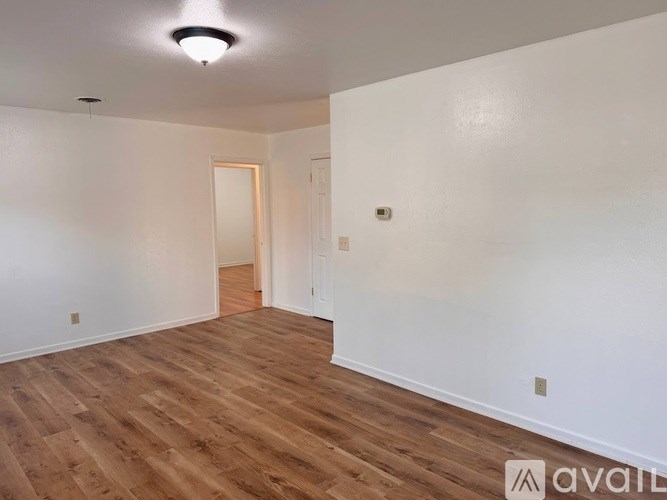 A room with wooden flooring and white walls, with a doorway leading to another room.