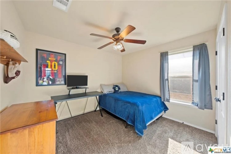 A bedroom with a bed, a table, a fan, and a TV.