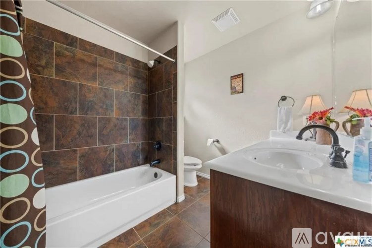 A bathroom with a brown tiled shower area and a white sink area.