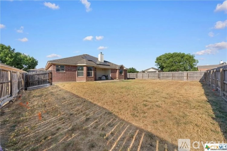 A backyard with a house, fence, and a grassy area.
