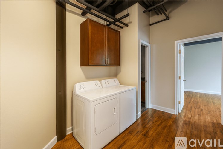 A white washing machine sits in a room with wood floors and a wooden cabinet above it.