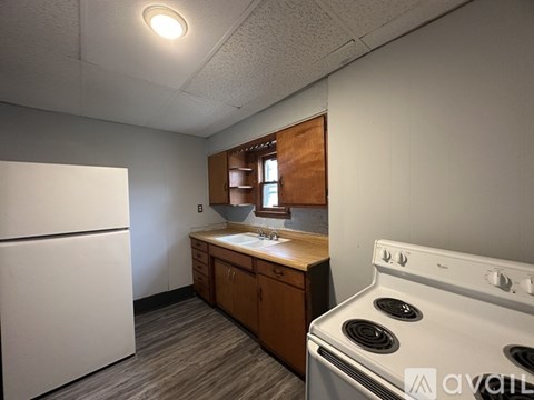 A small kitchen with a white fridge, wooden cabinets, and a white stove.