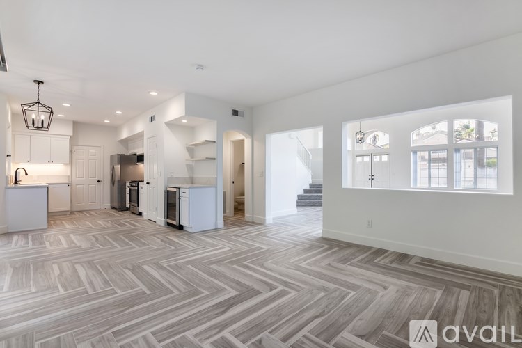 A spacious living room with a herringbone patterned floor and a kitchen area in the background.