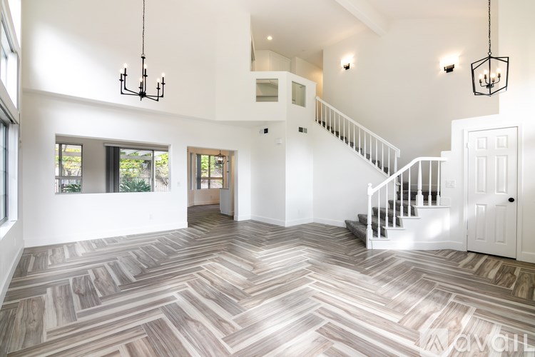 A spacious room with a herringbone patterned floor and a staircase.