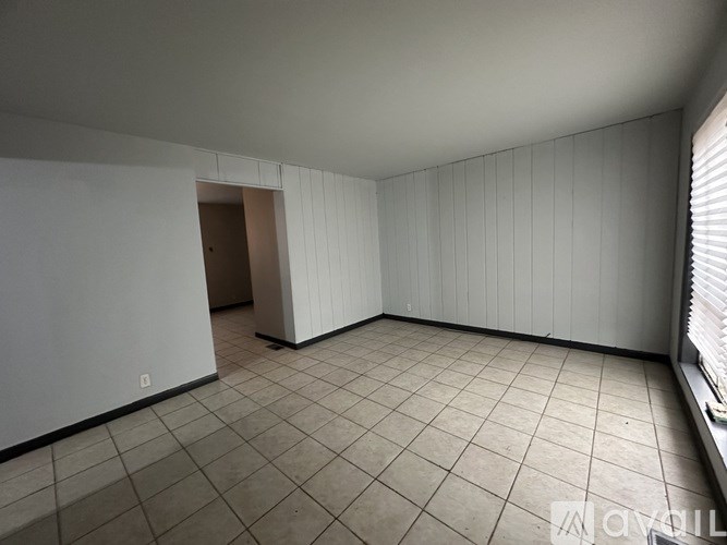 A room with white walls and a tiled floor with a doorway leading to another room.